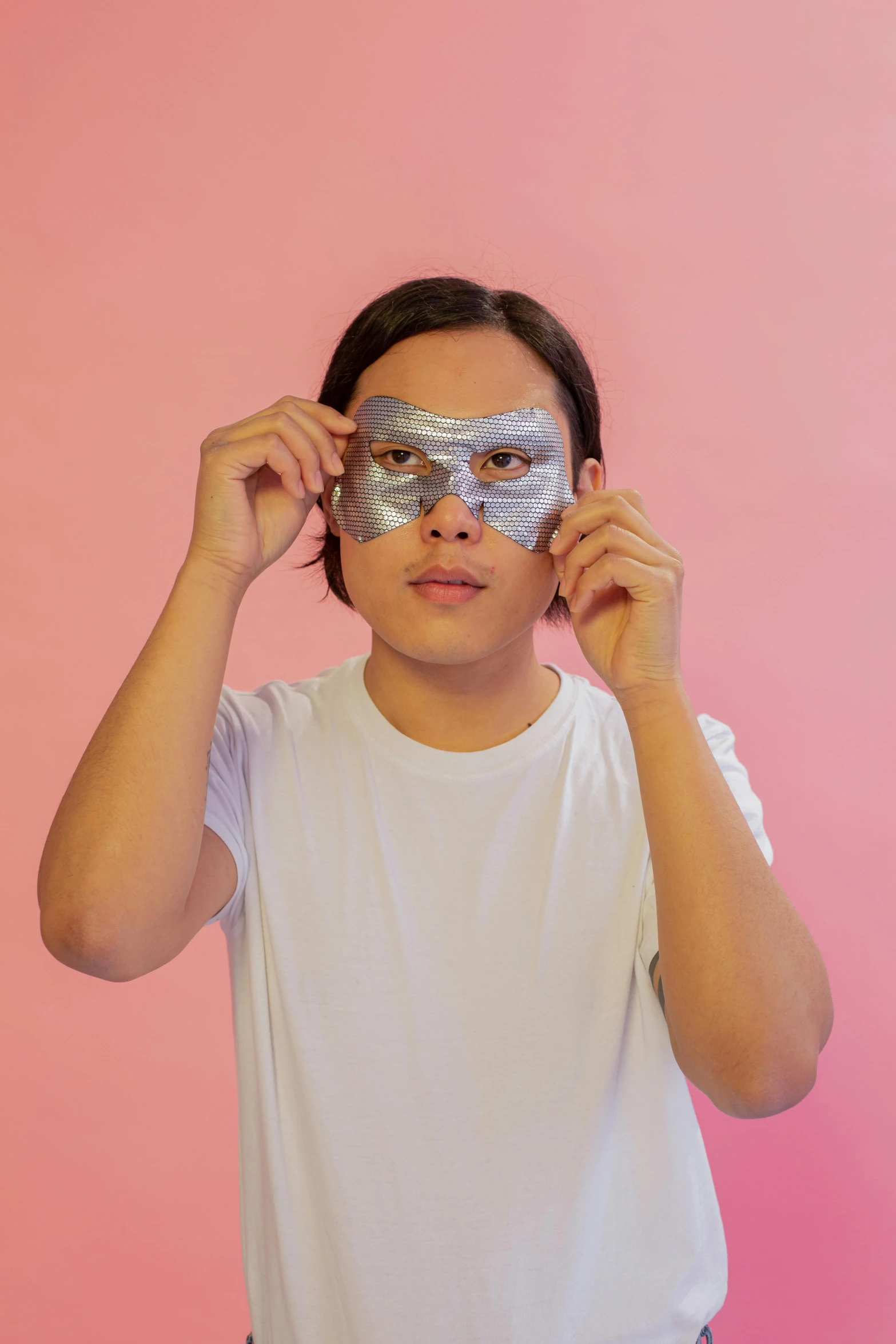 a man standing in front of a pink wall with a silver mask on his face, happening, bags under eyes, glass skin, genderless, asian male