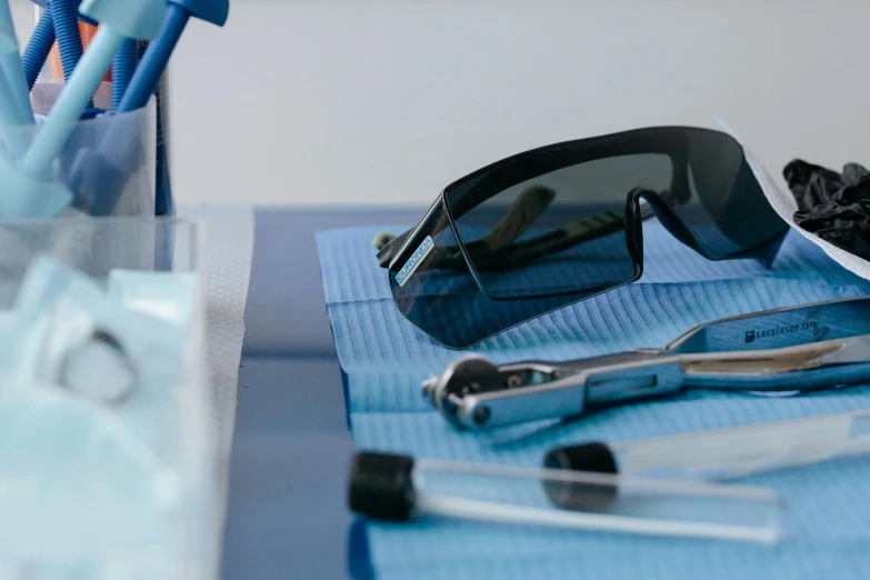 a pair of sunglasses sitting on top of a table, surgical implements, blue and black scheme, healthcare worker, dentist