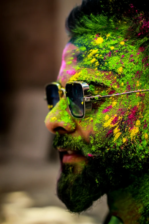 a man with green and pink paint on his face, an album cover, inspired by Steve McCurry, trending on pexels, cool sunglasses, bearded, celebration, extreme bokeh