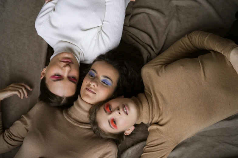 a group of women laying on top of a couch, trending on pexels, three heads, makeup, brown clothes, color block