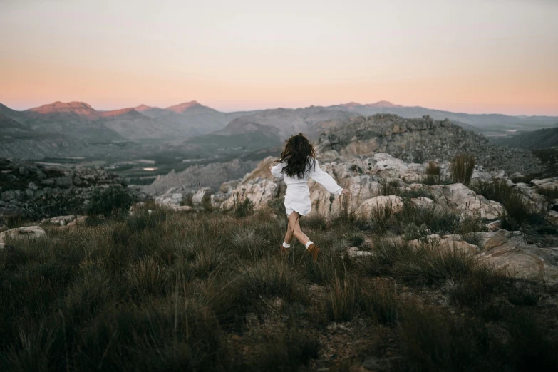 a woman in a white dress standing on top of a mountain, by Lee Loughridge, pexels contest winner, happening, girl running, early evening, various posed, unkept hair