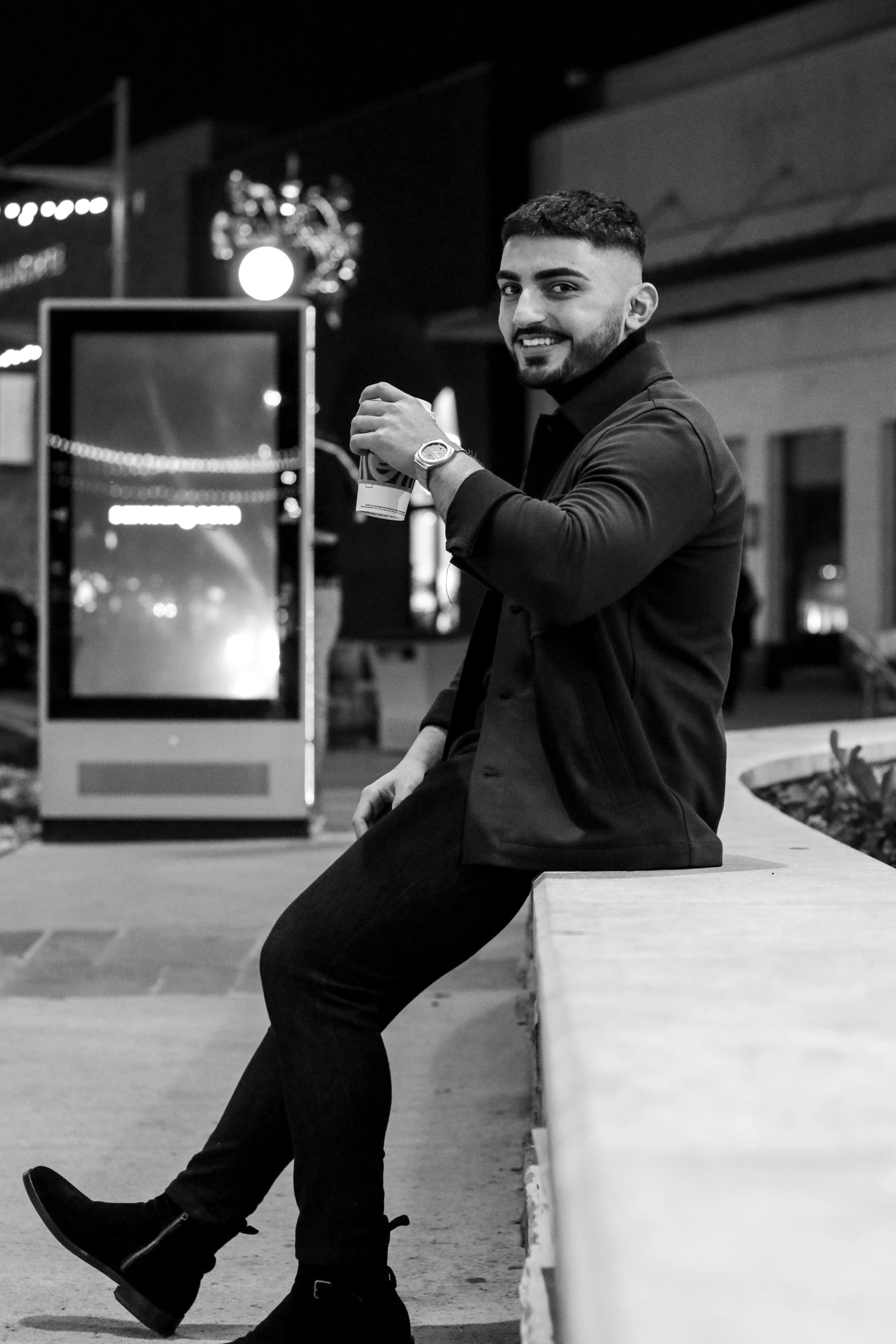 a black and white photo of a man sitting on a ledge, by Ismail Acar, wearing a track suit, night life, wearing a dark shirt and jeans, kyza saleem