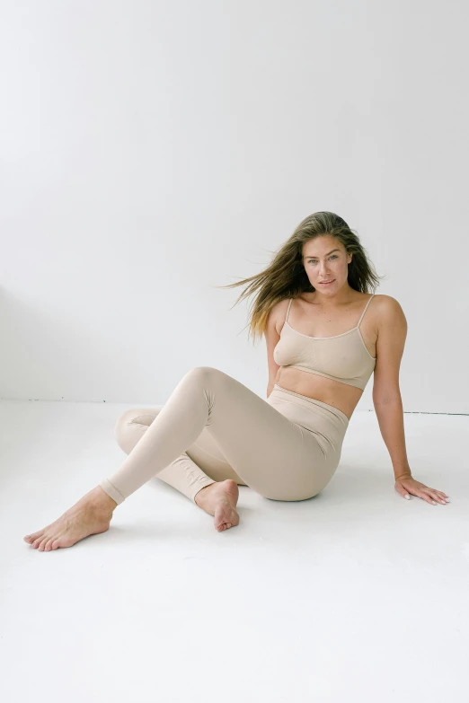 a woman sitting on the floor in a white room, two piece workout clothes, natural muted tones, on display, breeches