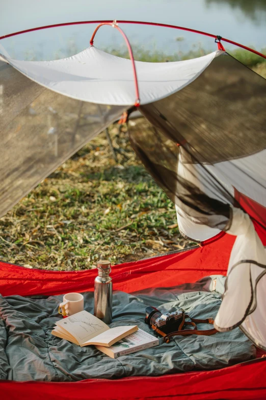 a person sitting in a tent reading a book, soft grey and red natural light, adventure gear, canopies, aerial shot