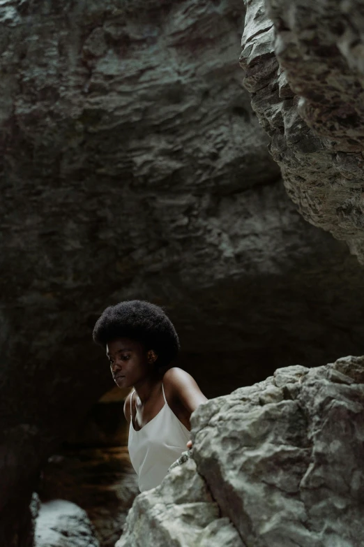 a woman sitting on top of a large rock, an album cover, inspired by Gordon Parks, pexels contest winner, hot springs hidden cave, natural hair, candid portrait photo, cave entrance