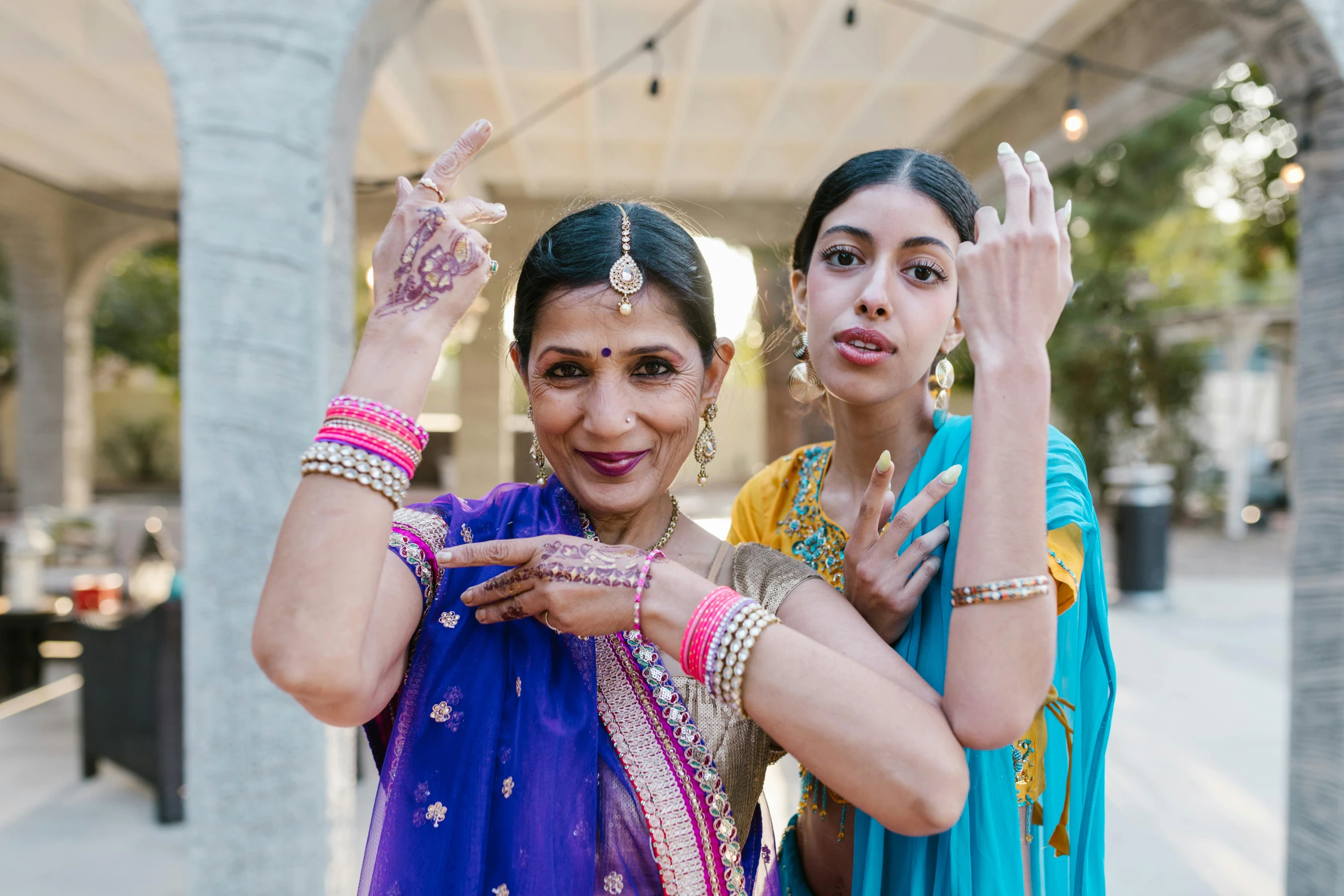 a couple of women standing next to each other, pexels, renaissance, bollywood, hands in the air, huge earrings and queer make up, california;