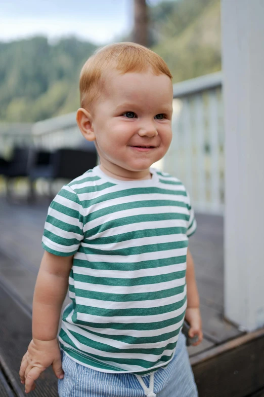 a little boy standing on top of a wooden deck, inspired by Robert Thomas, unsplash, wearing stripe shirt, jade green, closeup - view, wearing a t-shirt