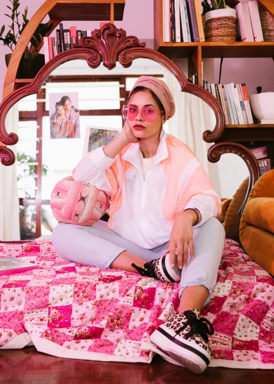 a woman sitting on a bed holding a baby, an album cover, by Julia Pishtar, trending on pexels, maximalism, wearing sunglasses and a cap, wearing a pastel pink hoodie, hindu aesthetic, androgynous person