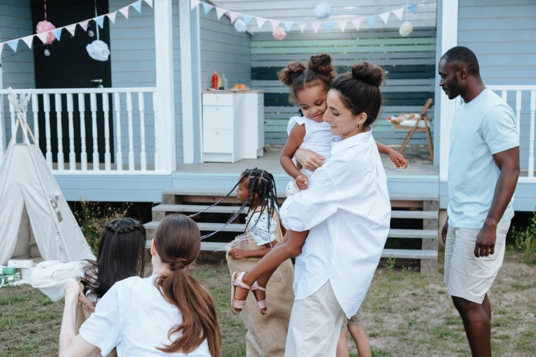 a group of people standing in front of a house, by Liza Donnelly, pexels contest winner, happening, woman holding another woman, at a birthday party, wearing a linen shirt, kids playing