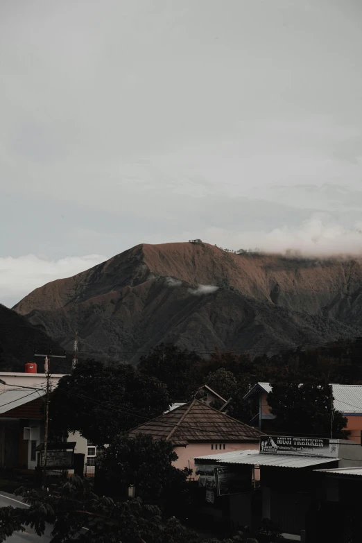 a small town with a mountain in the background, a picture, unsplash contest winner, sumatraism, overcast gray skies, manuka, ☁🌪🌙👩🏾, brown