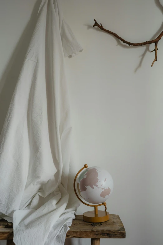 a globe sitting on top of a wooden table, white clothes, in a white boho style studio, low quality photo, two hang