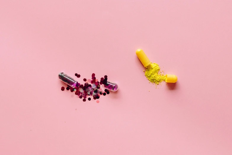 a couple of pills sitting on top of a pink surface, a picture, by Alexis Grimou, trending on pexels, black and yellow and red scheme, spilling juice, yellow purple green, pink lipstick