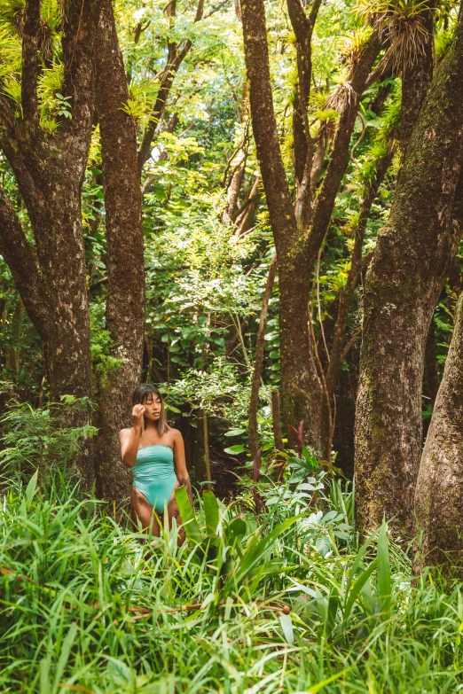 a woman walking through a lush green forest, inspired by Elsa Bleda, unsplash, green swimsuit, kauai springtime, wide angle full body, sitting under a tree