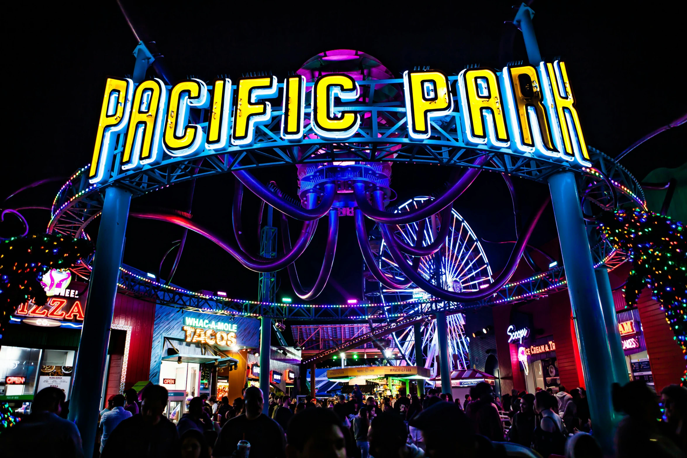 the entrance to pacific park lit up at night, by Julia Pishtar, outdoor rave, roller coasters, black neon lights, avatar image