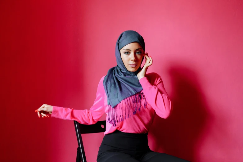 a woman sitting on a chair talking on a cell phone, inspired by Nazmi Ziya Güran, hurufiyya, hot pink, hijab, grey, promotional photoshoot