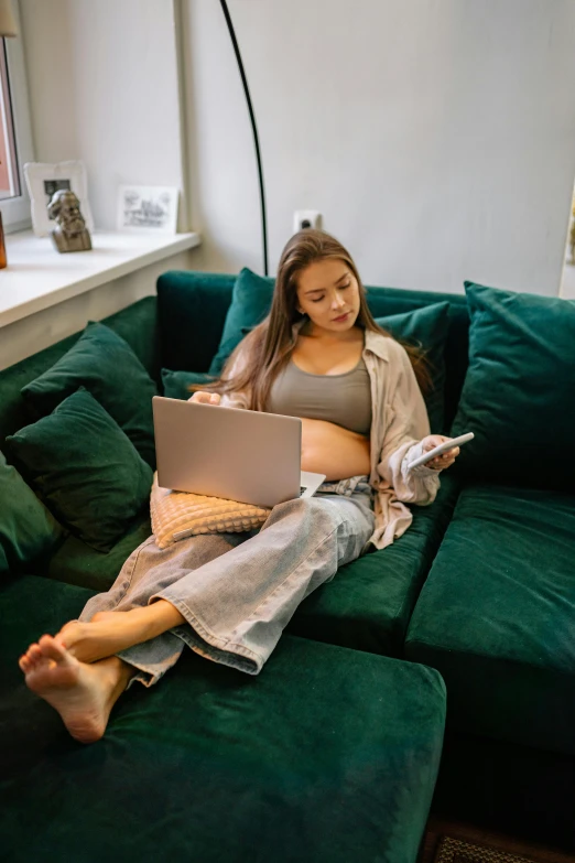 a woman sitting on a green couch using a laptop, trending on pexels, happening, pregnant belly, young asian woman, ( 3 1, full body