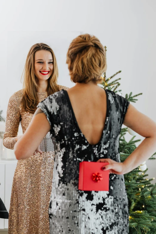 two women standing in front of a christmas tree, happening, profile image, sequin top, giving gifts to people, grey