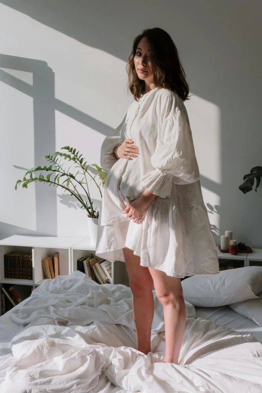 a woman in a white dress standing on a bed, inspired by Elsa Bleda, pexels contest winner, renaissance, maternity feeling, long shirt, side view of her taking steps, relaxed style