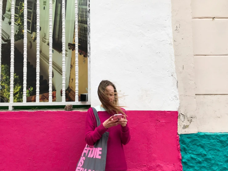 a woman leaning against a wall using a cell phone, a photo, by Gina Pellón, pexels contest winner, magenta colours, quirky shops, amanda lilleston, having a good time