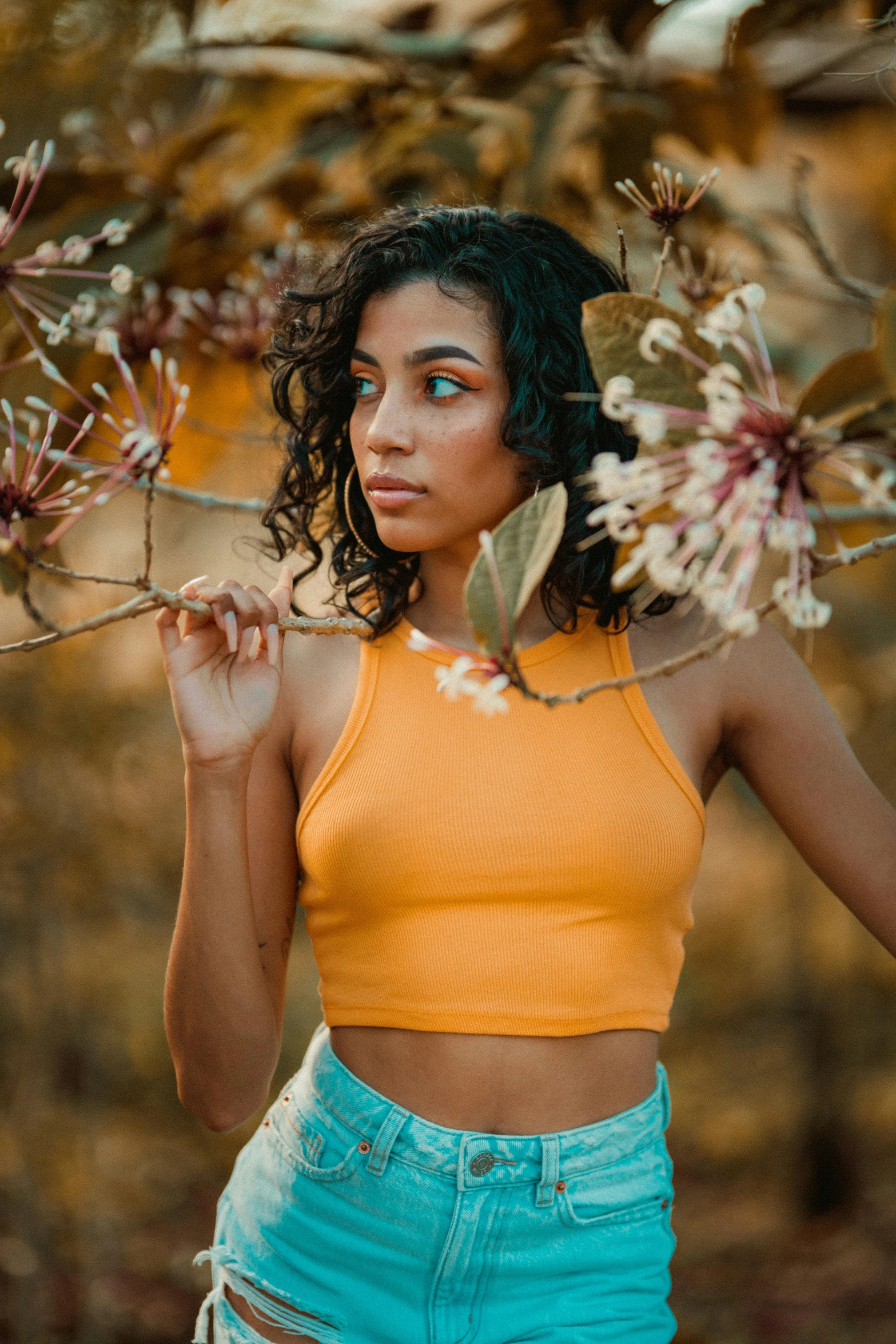 a woman standing in front of a tree with flowers, inspired by Elsa Bleda, trending on pexels, renaissance, wearing yellow croptop, mixed-race woman, orange halter top, wearing tight simple clothes