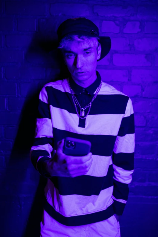 a man standing in front of a brick wall holding a cell phone, an album cover, unsplash, black light, lil peep, ((purple)), with hat