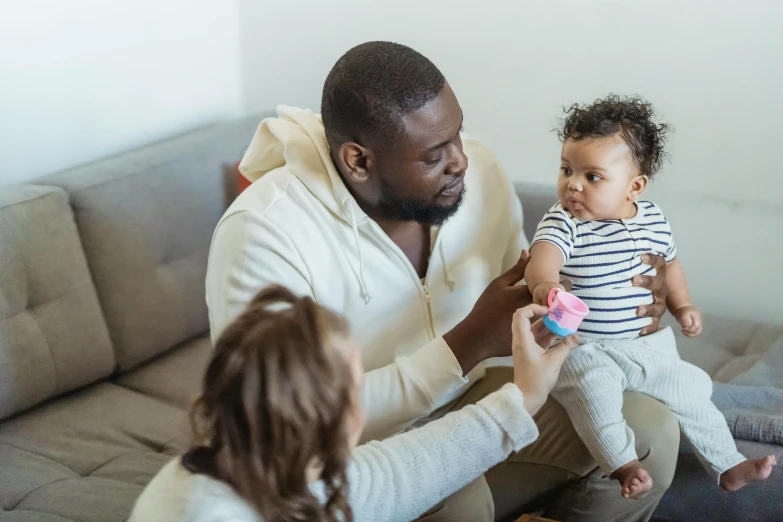 a man sitting on a couch holding a baby, pexels contest winner, incoherents, varying ethnicities, 1 4 9 3, holding an epée, small