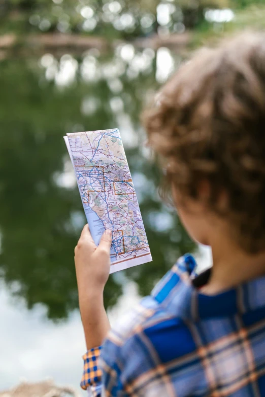 a person holding a map near a body of water, kid, center of interest, up close, varying locations