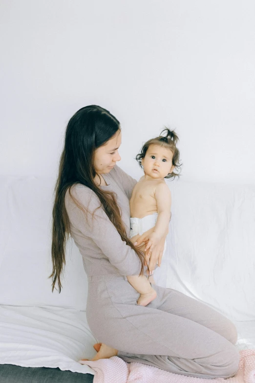 a woman sitting on a bed holding a baby, pexels contest winner, minimalism, muted colored bodysuit, 1 4 9 3, pokimane, medium head to shoulder shot