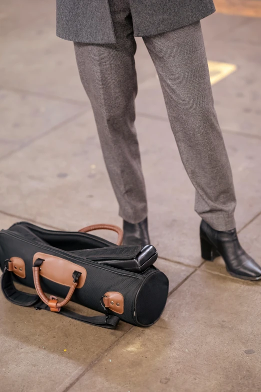 a man standing next to a suitcase on a sidewalk, trending on pexels, grey pants and black dress shoes, business woman, carrying a rifle, high angle close up shot