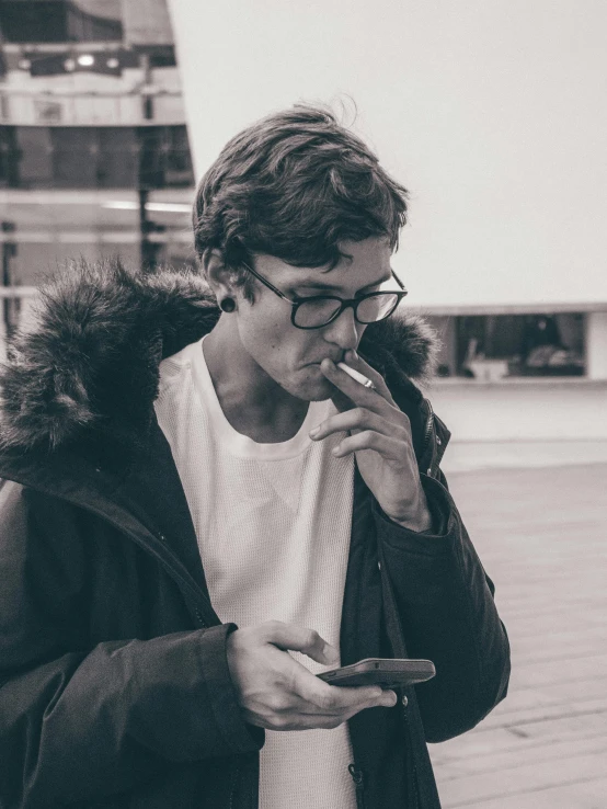 a black and white photo of a man smoking a cigarette, pexels contest winner, aestheticism, he looks like tye sheridan, he is holding a smartphone, discord profile picture, model wears a puffer jacket