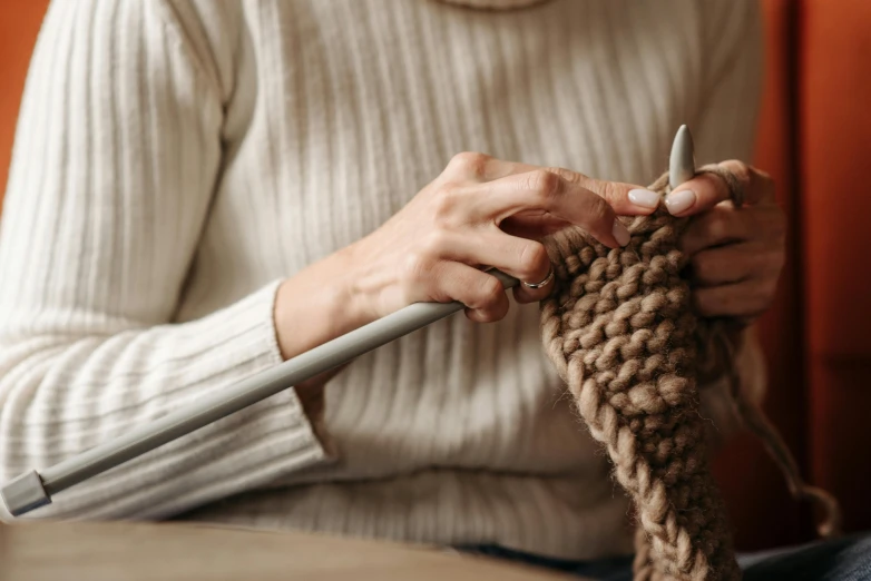 a close up of a person knitting a piece of yarn, by Elizabeth Durack, trending on pexels, brown sweater, holding a wooden staff, avatar image, multi-part