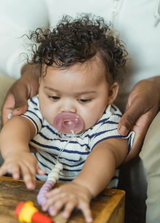 a woman holding a baby with a pacifier in her mouth, head straight down, diverse, connectivity, curls