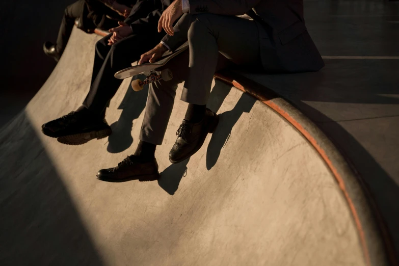 a group of people sitting on top of a skateboard ramp, by Bertram Brooker, trending on unsplash, photorealism, subject detail: wearing a suit, detailed with shadows, leather shoes, evening light