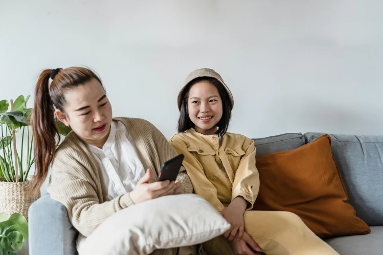 a couple of women sitting on top of a couch, a cartoon, trending on pexels, asian man, brown clothes, cellphone, lgbtq