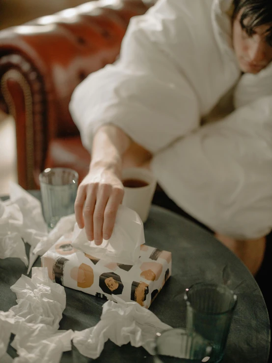 a person sitting at a table with a box of tissues, a marble sculpture, by Elsa Bleda, pexels contest winner, drinking cough syrup, dirty linen robes, gif, thumbnail