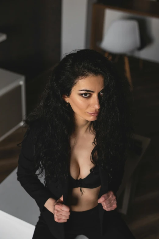 a woman sitting on top of a white table, long black curly hair, in a black betch bra, portrait featured on unsplash, a man wearing a black jacket