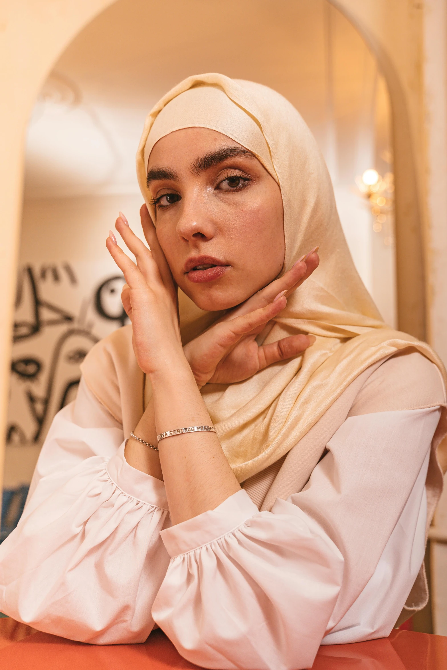 a woman sitting at a table with her hands on her face, inspired by Maryam Hashemi, hurufiyya, looking in mirror, white hijab, dua lipa, ( ( theatrical ) )