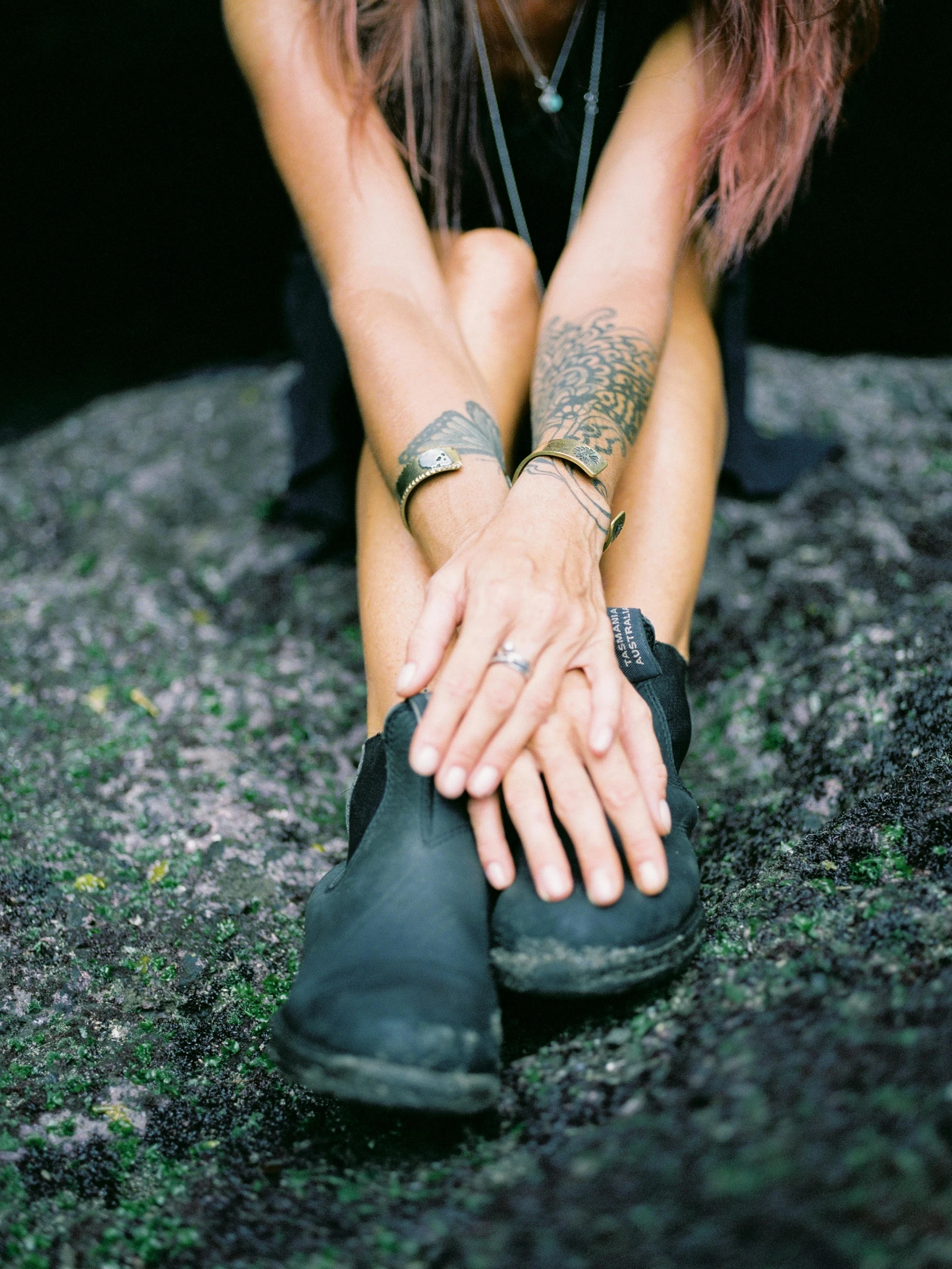 a woman sitting on a rock with her hands on her knees, a tattoo, trending on unsplash, boots, shungite bangle, low quality photo