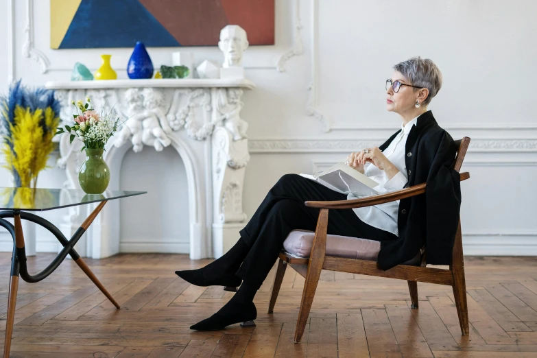 a woman sitting in a chair reading a book, inspired by Alexander Roslin, visual art, in suit with black glasses, mid-century modern furniture, non binary model, 30-year-old french woman