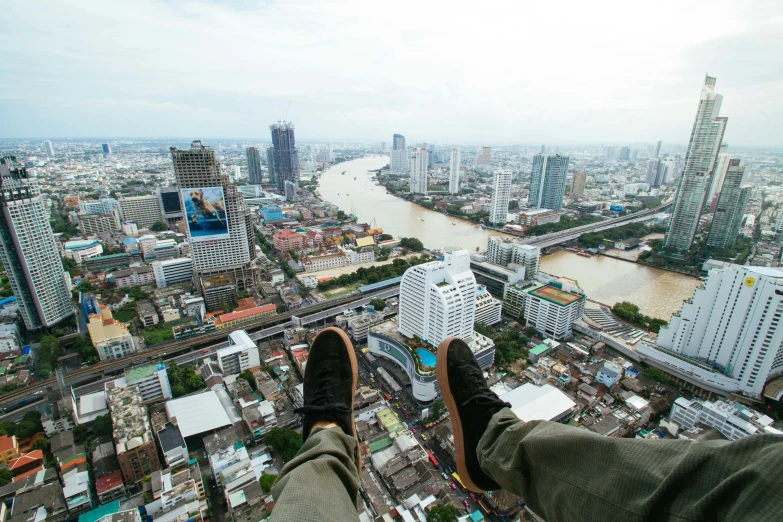 a person sitting on top of a tall building, pexels contest winner, hyperrealism, bangkok, feet on the ground, helicopter footage over city, sky bridge