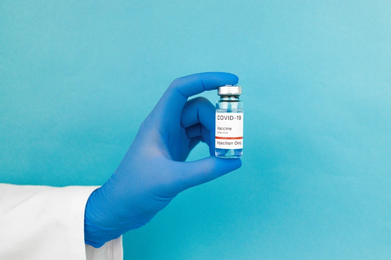 a person in a lab coat holding a vial, blue background colour, covid, instagram picture, blue gloves