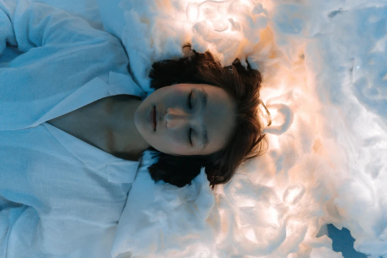 a woman laying on top of a bed covered in white sheets, inspired by Elsa Bleda, pexels contest winner, surrealism, detailed glowing head, face made out of clouds, an asian woman, gif