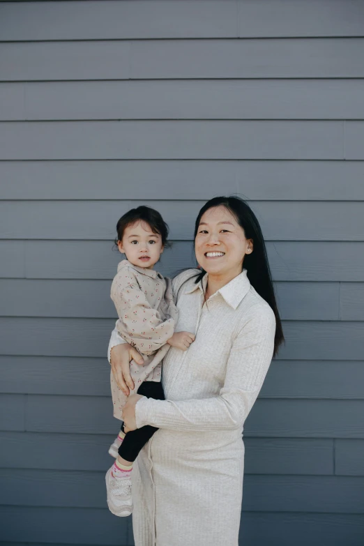 a woman holding a baby in her arms, unsplash, minimalism, asian descent, in front of a garage, gray canvas, square