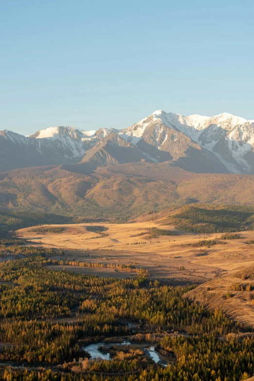 a view of a valley with mountains in the background, west slav features, golden glow, murata range, long shadows