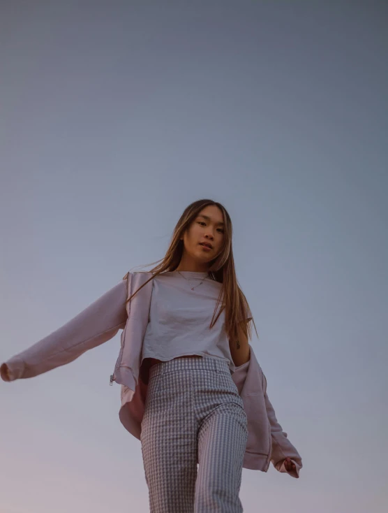 a woman standing on top of a beach next to the ocean, by helen huang, trending on unsplash, happening, wearing a light - pink suit, she is wearing streetwear, low angle facing sky, young asian girl