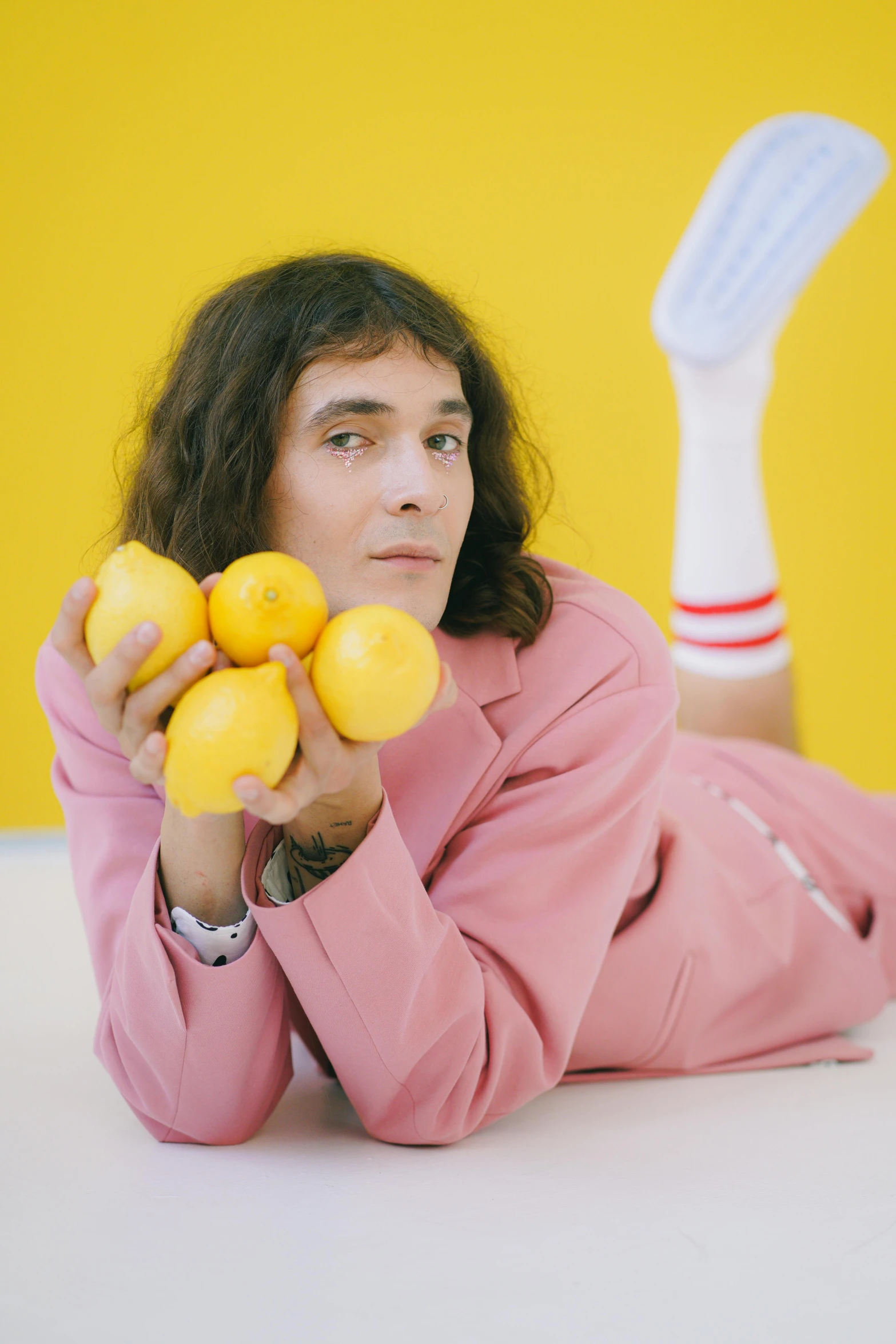 a man laying on the floor holding a bunch of lemons, an album cover, inspired by David LaChapelle, trending on pexels, wearing a light - pink suit, robert sheehan, andy milonakis, tommy wiseau