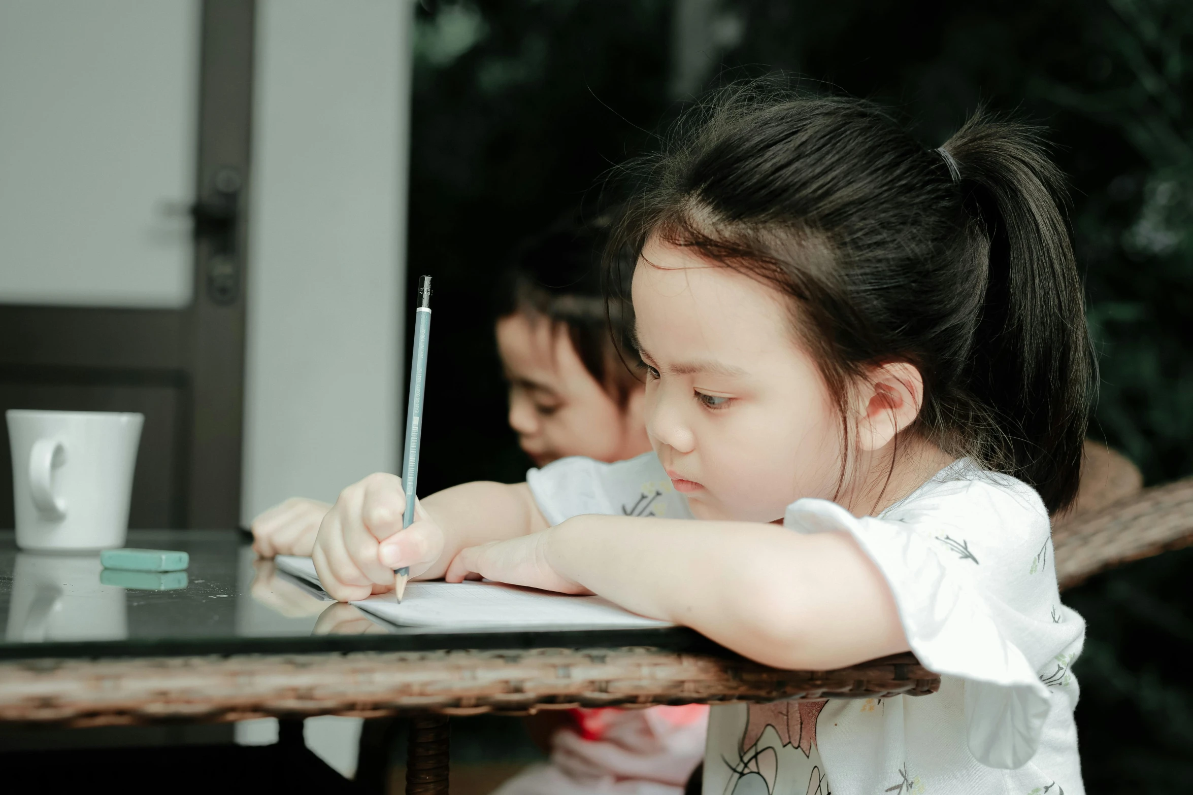 a little girl sitting at a table writing on a piece of paper, pexels contest winner, two girls, background image, looking her shoulder, asian girl