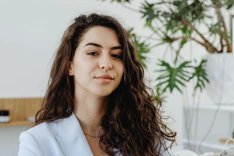 a woman sitting on a couch next to a potted plant, a character portrait, pexels contest winner, no makeup wavy hair, middle eastern skin, on a white table, headshot profile picture