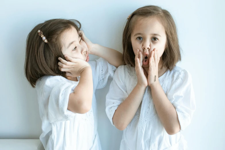 a couple of little girls standing next to each other, pexels contest winner, happening, speak no evil, wearing white pajamas, round teeth and goofy face, looking in mirror