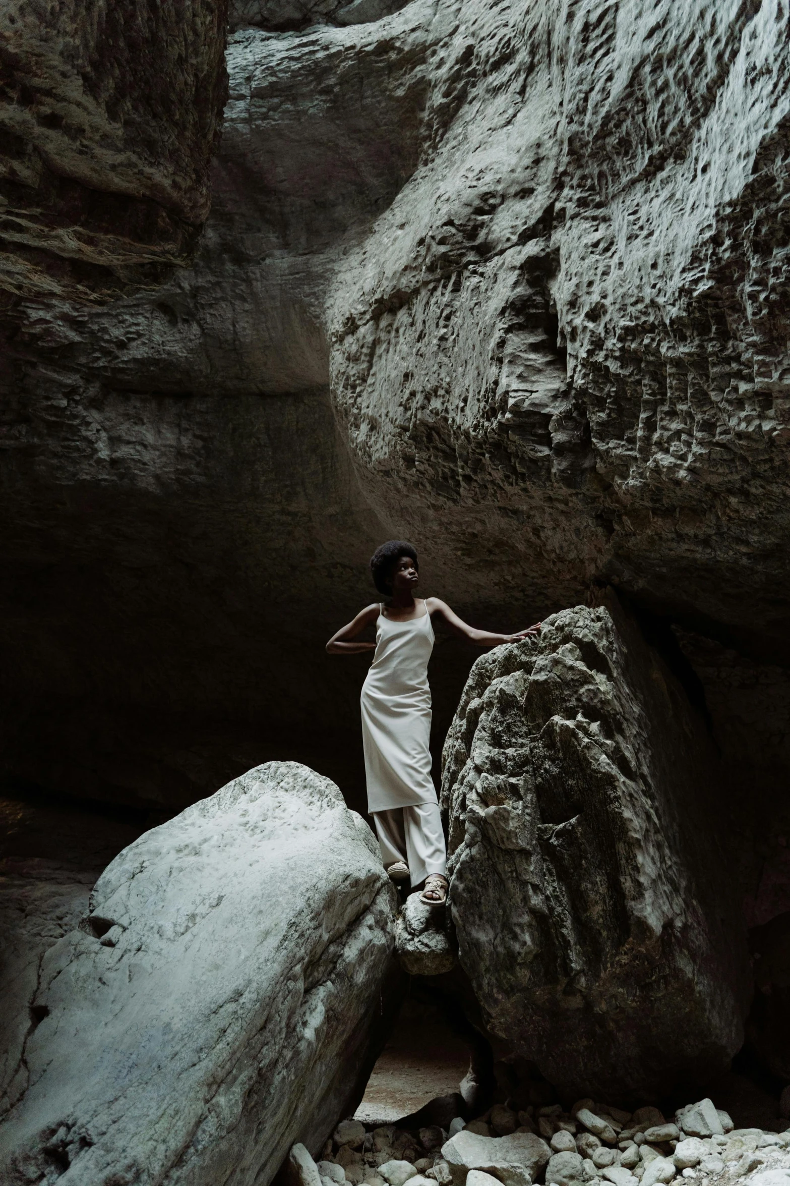 a woman in a white dress standing on a rock, inspired by Annie Leibovitz, unsplash contest winner, renaissance, found in a cave made of clay, 35 mm photo, black in, sandstone